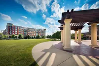 Elegant apartment complex with modern architecture, surrounded by lush green lawns and a stylish pergola under a bright blue sky.