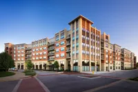 Modern apartment building with a brick facade, large windows, and private balconies, set in a beautifully landscaped urban area.