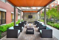 Chic outdoor lounge with modern wicker chairs, shaded pergola, and cozy fire pit, perfect for entertaining.