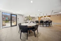 Modern communal dining area with elegant round table, stylish chairs, and a chic bar setup with contemporary lighting.