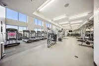 Bright and spacious gym with state-of-the-art equipment, large windows, and ample natural light in a modern apartment building.