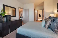 Elegant bedroom with plush bedding, modern dresser, and a glimpse into a stylish ensuite bathroom and cozy living area.
