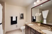 Elegant bathroom featuring dual sinks with granite countertops, dark wood cabinetry, and a luxurious bathtub with a modern tile design.