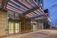 Modern apartment entrance with sleek glass facade and geometric canopy design at twilight.