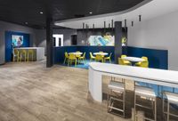Modern dining area with sleek yellow chairs, round tables, and contemporary artwork, complemented by stylish wood flooring and a chic, minimalistic design.