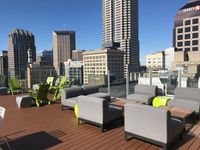 Stunning urban rooftop lounge with stylish seating and panoramic city skyline views under a clear blue sky.
