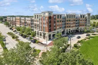 Modern apartment complex featuring stylish architecture with a blend of brick and stone exteriors, set in a vibrant urban environment surrounded by lush greenery and ample parking.