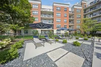 Chic urban apartment exterior with stylish lounge chairs and elegant umbrellas on a stone patio, surrounded by lush greenery.