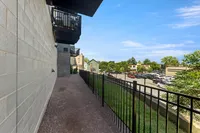 Charming urban balcony view with contemporary railing overlooking a sunlit neighborhood and lush trees.
