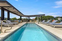 Luxurious rooftop pool surrounded by modern lounge chairs and stylish pergola, perfect for relaxation and leisure.