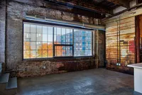 Chic industrial loft featuring exposed brick walls, large windows with city views, and rustic wooden elements.