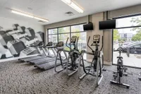 Modern fitness center with state-of-the-art treadmills, ellipticals, and exercise bikes, featuring large windows and a sleek dumbbell mural.