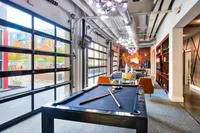 Chic urban lounge with a pool table, modern seating, and vibrant outdoor views through large glass doors.