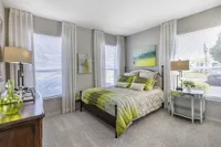 Bright and elegant bedroom featuring a plush bed with green accents, modern decor, and large windows inviting natural light.