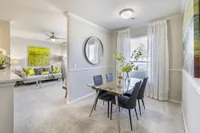 Bright and elegant dining area with a modern glass table and chic decor leading to a cozy, inviting living room with stylish accents.