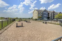Pet-friendly apartment complex featuring a spacious fenced dog park with agility equipment and stunning blue skies.