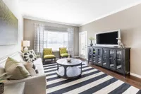 Elegant living room with natural light, chic striped rug, stylish sofa, and vibrant green accent chairs.