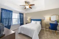 Bright and inviting bedroom with elegant decor, featuring a cozy bed, stylish blue accents, and natural light filtering through large windows.