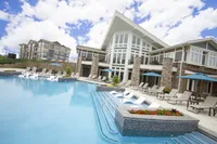 Luxurious apartment complex with a stunning outdoor pool, stylish lounge chairs, and elegant architecture, all under a bright blue sky.