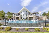 Luxurious apartment complex with a stunning outdoor pool, elegant stone facade, and modern design elements under a clear blue sky.