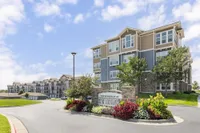 Charming multi-story apartment complex with modern architecture, surrounded by lush landscaping and vibrant flower beds under a clear blue sky.