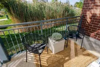 Charming apartment balcony with modern black chairs, a woven rug, and lush greenery views.