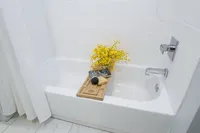 Elegant bathroom featuring a pristine white bathtub with a luxurious wooden bath tray, accented by vibrant yellow flowers and spa essentials for a relaxing atmosphere.