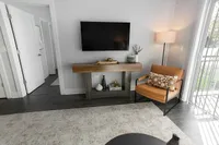 Contemporary living room with sleek accents featuring a wall-mounted TV, inviting leather chair, and stylish console table, complemented by warm lighting and a view of lush greenery outside.