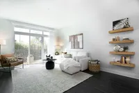 Elegant living room with modern white sofa, stylish decor on wooden shelves, and large windows offering a bright airy feel.