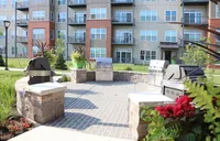 Modern apartment exterior with stylish balconies, landscaped greenery, and a communal grilling area.