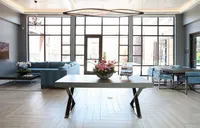 Bright modern living space with large windows, elegant chandelier, and stylish seating area featuring a plush blue sofa and sleek dining table.