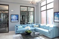 Bright and elegant living room with large windows, featuring a plush blue sectional sofa, chic chandelier, and modern artwork.