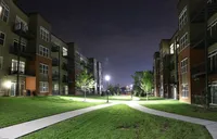 Elegant apartment complex with modern design, illuminated at night, featuring well-maintained green spaces and pathways, offering a serene and upscale living environment.