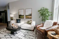 Chic living room boasting a modern white sofa, elegant leather chair, tasteful artwork, and lush greenery, bathed in natural light.