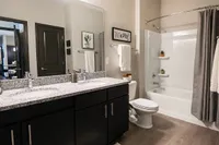 Modern bathroom with elegant double vanity, granite countertops, and a sleek shower bathtub in stylish apartment setting.