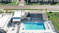 Aerial view of a modern residential complex featuring a sparkling blue pool, stylish lounge area, and surrounding green lawns.