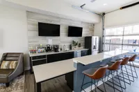 Modern kitchen space with sleek countertops, stylish bar seating, dual wall-mounted TVs, and top-notch appliances.
