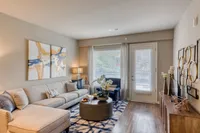 Inviting living room with elegant décor, featuring a cozy sectional sofa, abstract wall art, and abundant natural light through large windows.