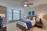 Elegant bedroom with a cozy bed, plush pillows, and modern decor, bathed in natural light from large windows.