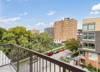 Charming cityscape view from a balcony overlooking lush trees and towering apartment buildings under a bright blue sky.