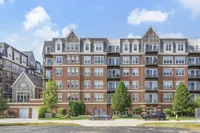 Elegant multi-story apartment building with modern brick design, large windows, and spacious balconies, surrounded by lush greenery and clear blue skies.