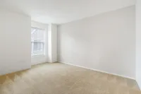 Bright, spacious room with a large window and plush beige carpet, perfect for personalization and comfort.