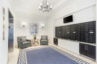 Elegant apartment lobby featuring a modern chandelier, cozy seating with two armchairs and a table, stylish wall sconces, and an organized mailroom with black mailboxes.