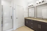 Elegant bathroom featuring a sleek glass shower, dual vanity with granite countertops, and modern lighting.