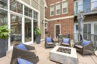 Chic outdoor patio with stylish wicker seating, vibrant plant accents, and a modern brick facade, offering a cozy and inviting retreat.