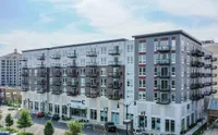 Contemporary six-story apartment building with modern facade and multiple balconies, set in a vibrant urban neighborhood.