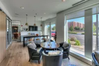 Modern apartment interior with sleek kitchen, cozy dining area featuring leather chairs, and large windows offering an expansive city view.