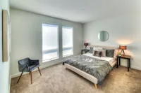 Bright and inviting bedroom with modern decor, featuring a cozy bed, elegant side tables with lamps, and a stylish chair by large windows for natural light.