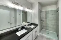 Modern bathroom featuring dual sinks with elegant fixtures, a sleek black countertop, and a spacious glass-enclosed shower.