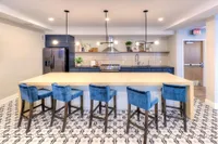 Chic modern kitchen with vibrant blue velvet chairs, spacious island, stylish pendant lights, and sleek stainless steel appliances on patterned tile flooring.